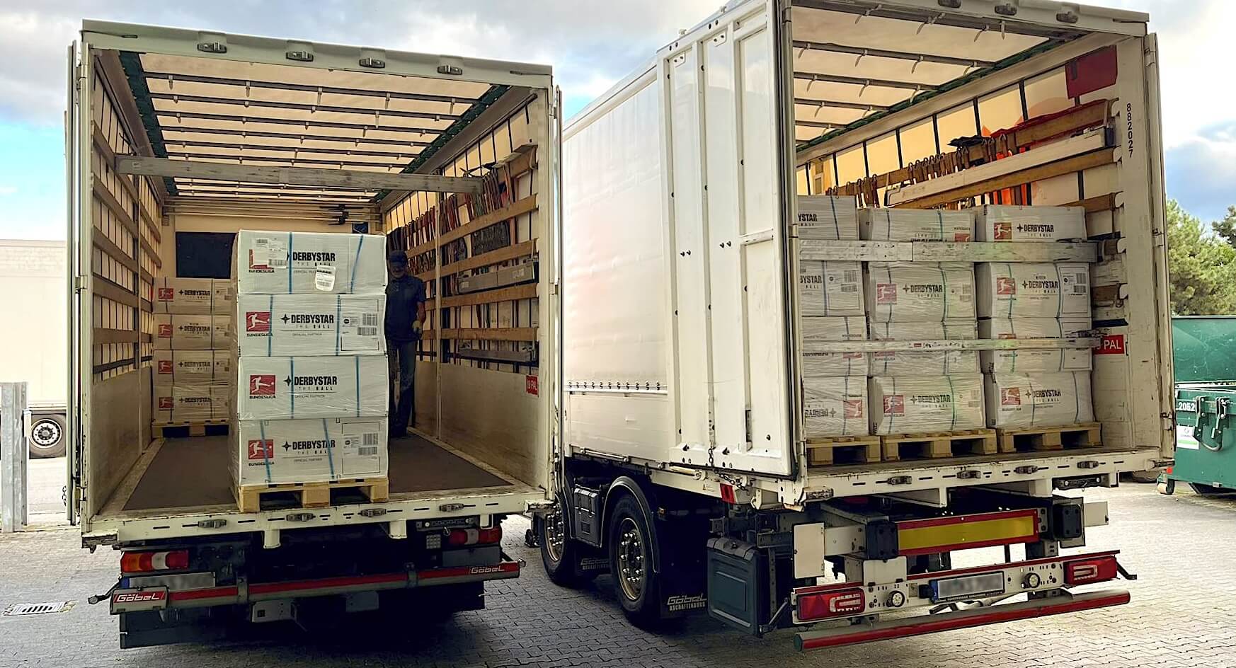 pickpack2_anlieferung_xs zwei lkws an einer landerampe mit blick auf die ladeflächen, die voller kartons und paletten sind